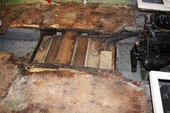 A boat's floor with no carpet and exposing the rotted wood floor.