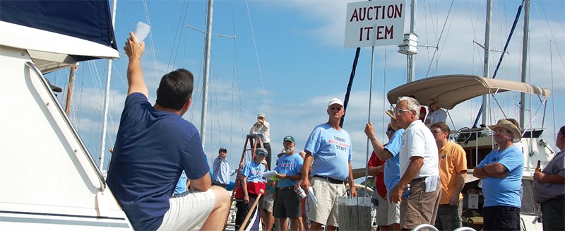 A boat auction taking place on a sunny day with many bidders around the boats.