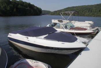 A few boats floating in the water in their boat slip on a sunny day with wodded hills in the background.