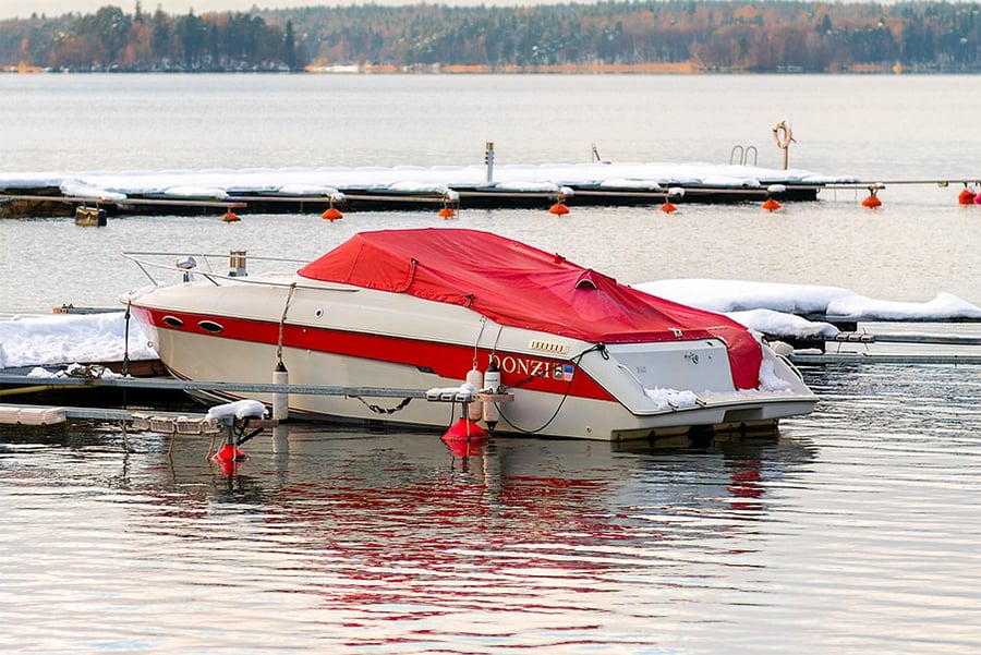 A red and white Donzi boat is the only boat left in the water in a marina with snow covering the docks.
