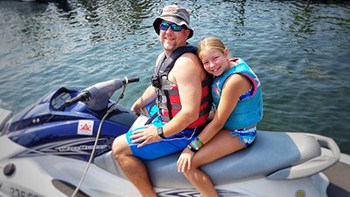 A man and his daughter sitting on a PWC (personal watercraft) floating in the water on a sunny day.