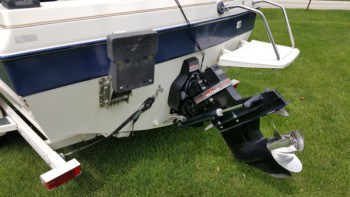 The back of a blue and white boat on it's trailer parked over grass with a focus on the outdrive.