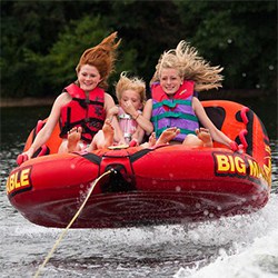 Three girls on a Big Mable tube airbourn above the water with trees in the background.