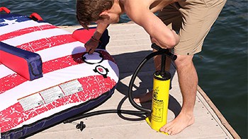 The AIRHEAD Double Action Hand Pump being used to inflate a towable tube on a dock.