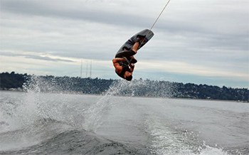 A wakeboarder inverted over a boat wake with cloudy skys in the background.
