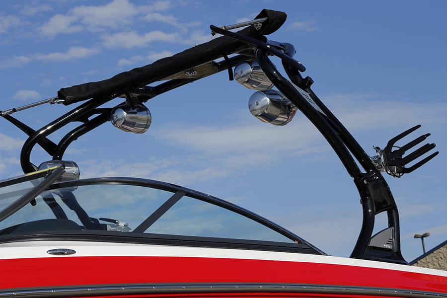 A black wakeboard tower mounted to a red and white boat with blue sky in the background.
