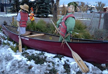 A canoe sitting in the leftover spring snow with fake people holding ores.