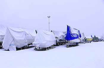 Boats stored outside with wraps and covers, with snow all over them.