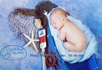 A photographer's photo of a baby sleeping in a little blue boat with nautical items displayed around it.