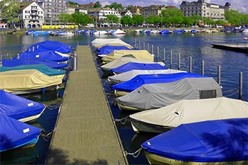 A marina with many boats at dock and all of them have covers on.