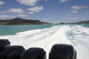 A set of four outboards looking backwards over the blue ocean with islands in the background.