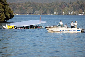 The New York state police boat arriving at a submerged pontoon boat out in a lake.