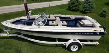 A fish and ski boat on a trailer on a sunny day showing the open bow can be used with a pedistal seat or as open floor for standing.