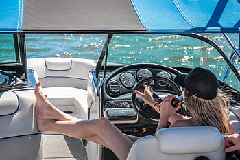 Looking from the stern of the boat forward, a woman driving a bowrider boat and drinking a beer on a sunny day.