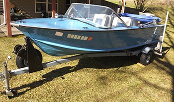 A 1960's era boat that is completely restored on a trailer in a yard on a sunny day.