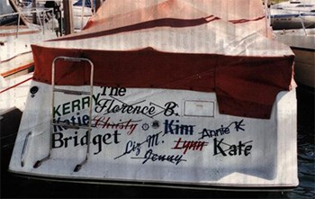 A boat at dock in a marina showing the transom with many women's names crossed off and one not crossed off.