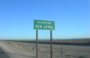 A road sign stateing elevation is sea level next to a a fence referencing that A combustion engine will run best at sea level.