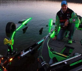 A man on a black and green boat floating next to a black boat trailer with green LED lighting which is the bluewater led trailer lighting kit.